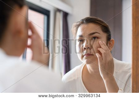 Middle Aged Asian Woman Looking At Wrinkles In Mirror