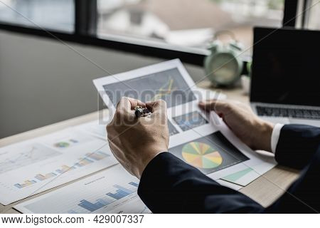 A Businessman Using A Pen To Point A Pie Chart On A Document, He Is Reviewing Financial Documents Fr