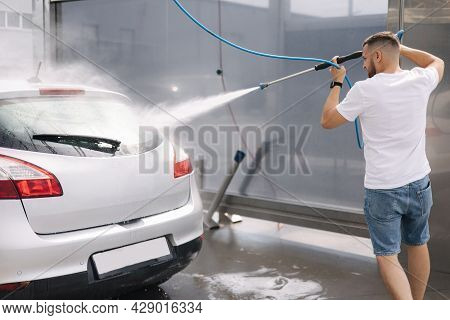 Back View Of Young Man Cleaning His Car With A Jet Sprayer. Self Service Car Washing