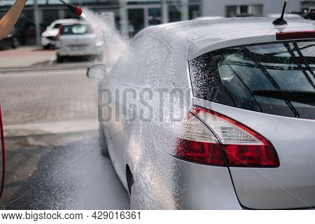 Back View Of Young Woman Cleaning Her Car On Self Service Car. Female Washing With Jet Sprayer. Whit