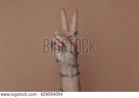 V Fingers Gesture, Hand Wrapped In A Metal Chain On A Brown Background. Suppression Of Freedom Or Im