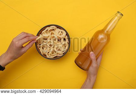 Female Hands Hold Beer And Snacks Corn Rings On Yellow Background
