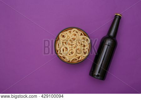 Beer Bottle And A Bowl With Corn Rings On A Purple Background. Top View