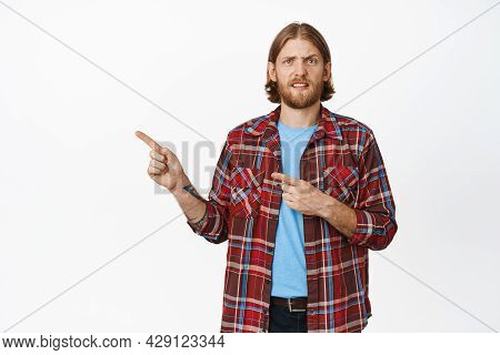 Portrait Of Confused Nervous Blond Man, Pointing Fingers Left And Frowning, Cringe In Doubt Disbelie
