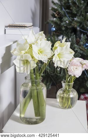 A Bouquet Of Pink Persian Buttercups In A Glass Vase And Two Wrapped Gifts On A White Table In Front