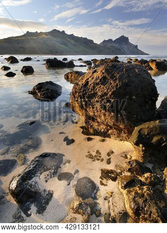 Rocks And Sunlight On The Coast Near Mountains On Beach