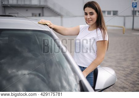 Attractive Happy Joyful Female Driver Wipe Windshield On Her Car Using Rag In Self-service Car Wash