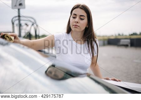 Attractive Happy Joyful Female Driver Wipe Windshield On Her Car Using Rag In Self-service Car Wash