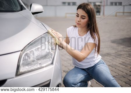 Front View Of Attractive Happy Joyful Female Driver Washing Her Cars Headlights With Special Rag In 