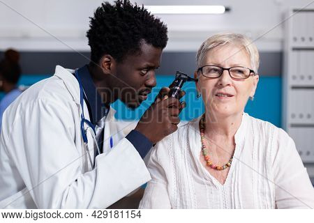 Black Young Doctor Using Otoscope On Elder Patient For Ear Consultation And Examination. African Ame