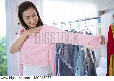 Attractive Asian Women Try A Pink Sweater In Front Of A Mirror Door Wardrobe At Home. The Clothes Ra
