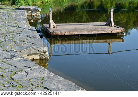 A Wooden Raft Is Tied To A Taut Rope. Self-service Ferry Across The River, Pond. People Get On And P