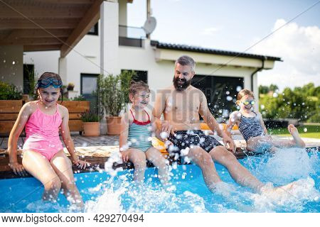 Father With Three Daughters Outdoors In Tha Backyard, Sitting By Swimming Pool.
