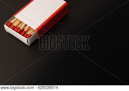 Black Background With An Open Matchbox In The Corner Of The Image. There Is A Blank White Label On T