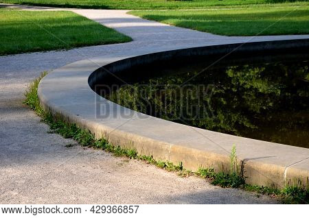 Edge Of A Stone Sandstone Circular Fountain In The Park. Built Of Sandstone Filled With Water. Lined