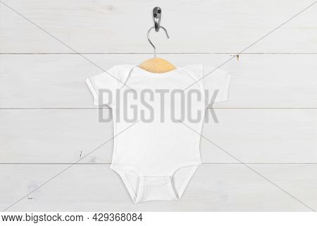 White Baby Onesie Hanging On A Tiny Wooden Hanger Against A Modern White Wood Wall.