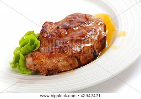 Gegrilltes Schweinesteak auf einem weißen Teller mit grünem Salat