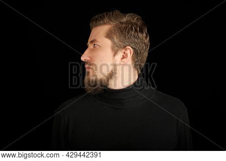 Cute Bearded Man, Half-face Portrait, Black Background. Young Guy In Black Polo Neck Sweater. Confid