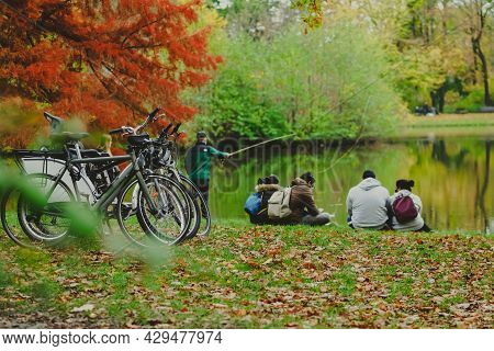 Parked Bicycles In Autumn Park And Group Of People Near Pond In City Park In A Rainy Autumn Day, Hor