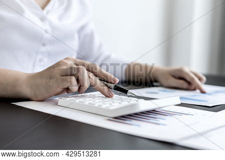 Close-up Of Woman Holding A Pen And Pressing A White Calculator, A Corporate Finance Auditor Examini