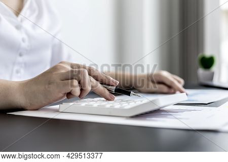 Close-up Of Woman Holding A Pen And Pressing A White Calculator, A Corporate Finance Auditor Examini