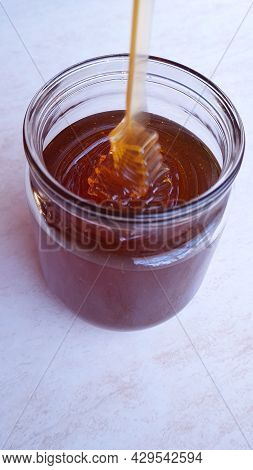 Honey Flowing Into A Glass Jar On A Light Background
