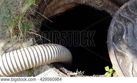 A Hose Is Lowered Into The Sewer Manhole To Pump Water Out Of The Pit. Cleaning Of The Sewer Pit. Ma