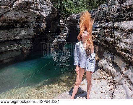 Longhaired Girl Throws Her Head Back While Standing By The Turquoise Water On The Rocky Shore Among 