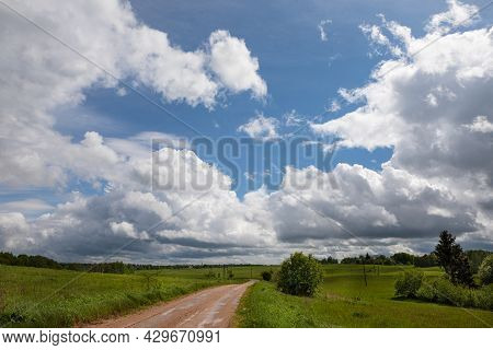 Rural Landscape With Unpaved Road And Green Pastures In The Summer. Big Skies With The Fluffy Cummul