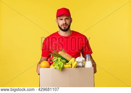 Online Delivery, Shopping And Food Order Concept. Doubtful And Upset Courier In Red Uniform Cap And 