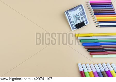 Colorful Art Supplies And Usd 100 Dollar Bills In A Paper Clip Arranged As A Side Border On A Beige 