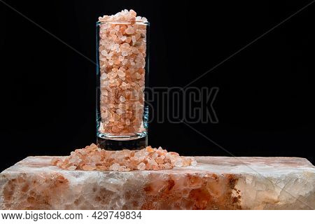 A Tall Glass Beaker Filled With Large Crystals Of Pink Himalayan Salt Stands On A Large Slab Of Hima