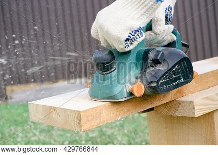 Carpenter Hands In Gloves Electric Plane Planing Lumber, Flying Shavings, Sawdust. Close-up On Glove