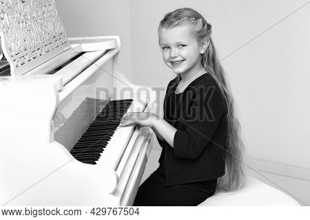 Beautiful Little Girl Playing On White Grand Piano. Black And White Shot Of Pretty Long Haired Girl 