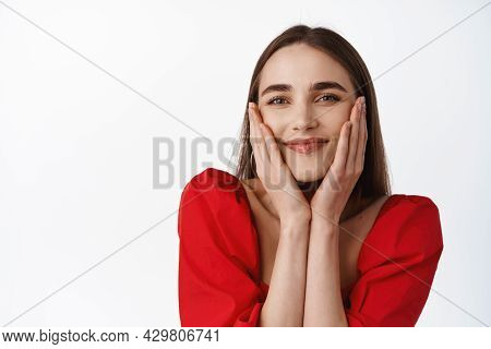 Close Up Portrait Of Pleased Happy Girl In Red Dress, Sqeeze Cheeks, Hold Hands On Face And Smiling 