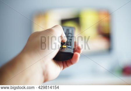 Out Of Focus And Blurry Close Up Male Hand Holding Remote Control Pointing To Change The Programme T