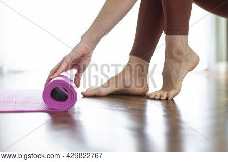 Young Woman Rolling Her Yoga Mat After Exercising And Doing Meditation At Home