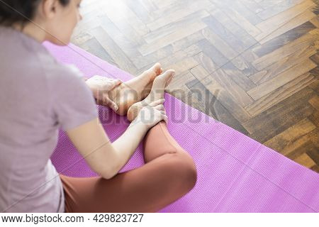 Young Woman In Sportswear Sitting On Youga Mat In Living Room And Doing Butterfly Stretch