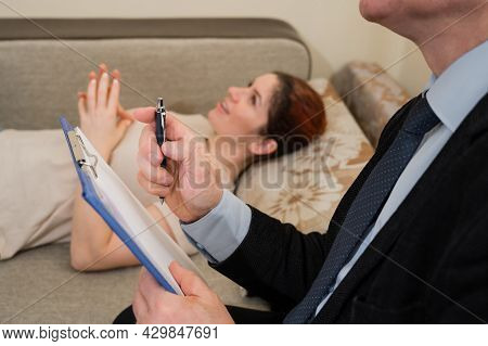 Caucasian Woman Lies On A Couch At A Reception With A Psychotherapist. An Elderly Man Works As A Psy