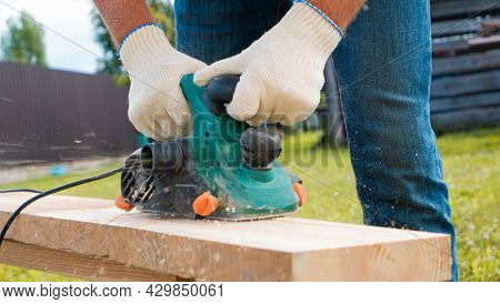Carpenter Hands In Gloves Electric Plane Planing Lumber, Flying Shavings, Sawdust. Close-up On Glove