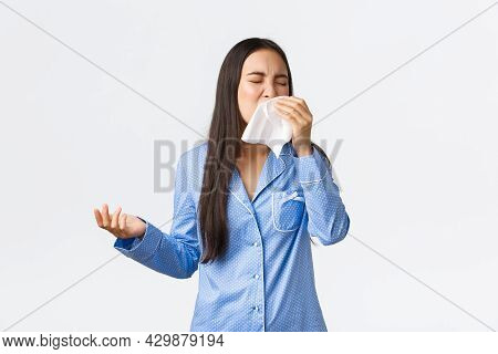 Asian Girl In Blue Pajamas Sneezing In Napking, Having Seasonal Allergy Or Got Sick, Staying Home Wi