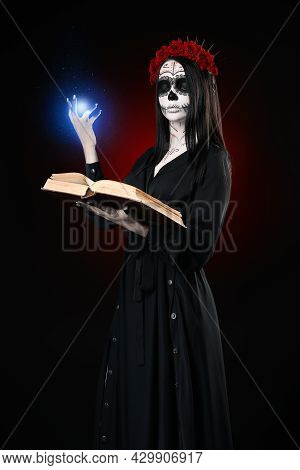 Young Woman With Calavera (sugar Skull) Makeup Holds Book (grimoire) And Casts The Spell. The Witch 