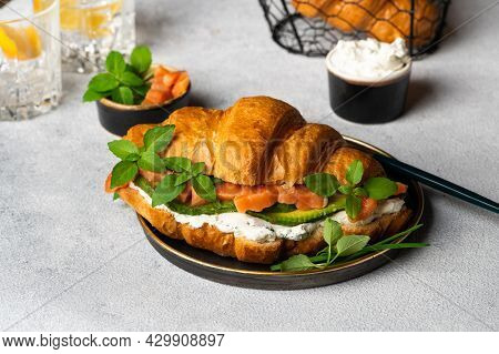 Croissant With Smoked Salted Salmon, Spinach And Arugula Served On Black Plate. Close Up. Healthy Fr