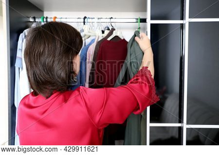Woman Choosing An Outfit From Her Wardrobe. Girl In Red Nightie Standing In Front Of Hanger Rack And