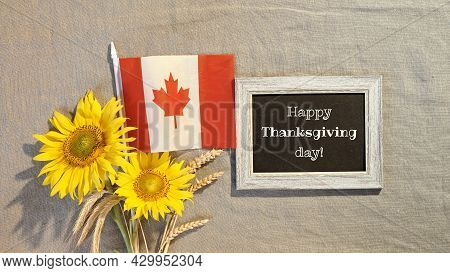 Happy Thanksgiving Text On Blackboard. Canada Flag With Sunflowers And Autumn Decorations. Flat Lay 