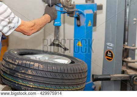 Mechanic Changing Tire In Car Service. Tire Rotation Machine.car Mechanic Mounts Tire On Wheel In A 