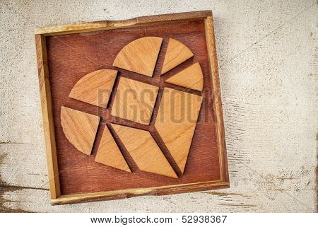 broken heart - tangram pieces in a box, a traditional Chinese Puzzle Game made of different wood parts to build abstract figures from them, on white painted barn wood