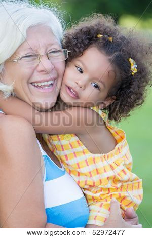 Grandmother hugs her hispanic granddaughter and laughs (with a diffused green grass background)