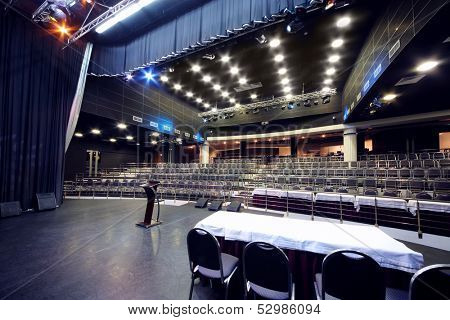 Document stand and table on stage and rows of seats in black hall for business meetings. 
