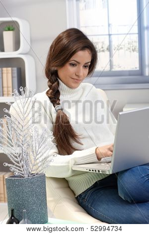 Portrait of attractive woman sitting at home using laptop computer, winter ambience.